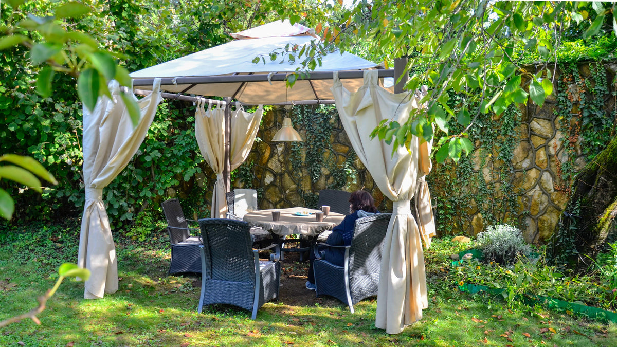 Garden gazebo with cream fabric curtains over a cushioned dining set