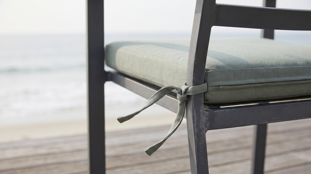 Outdoor chair cushion tied to an aluminum chair rail with matching fabric ties on a breezy coastal deck