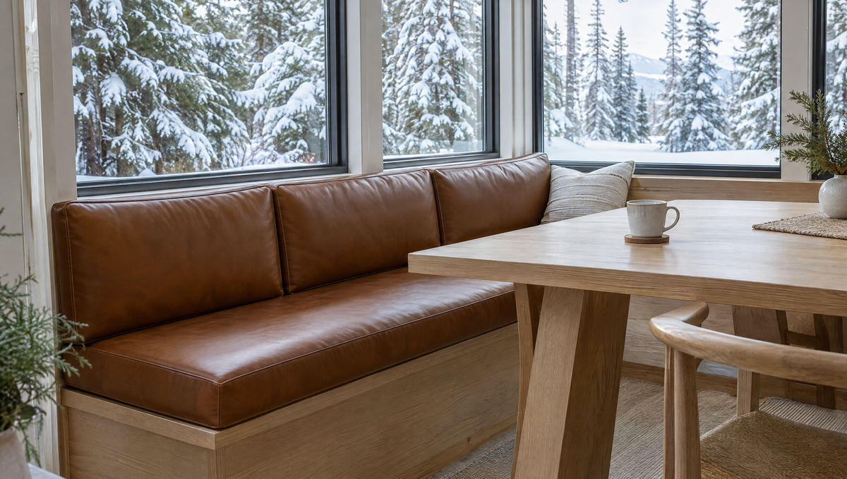 Banquette bench with cognac faux leather cushions in a bright sunroom with snowy pine trees outside