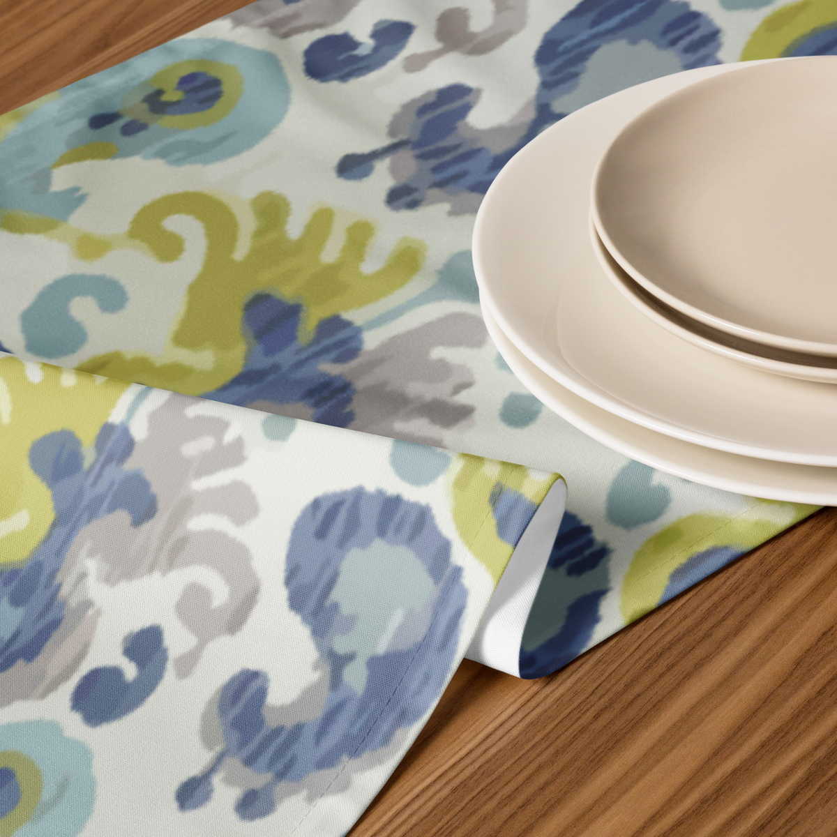 Ikat-print table runner in blue and green beneath stacked cream plates